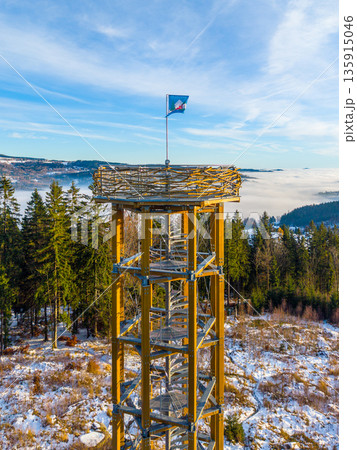 Svetly vrch lookout tower stands tall against a winter sky in Albrechtice. Snow covers the ground and trees surround the area. A flag flutters at the top of the tower. Svetly vrch lookout tower stands tall against a winter sky in Albrechtice. Snow covers the ground and trees surround the area. A flag flutters at the top of the tower. 135915046