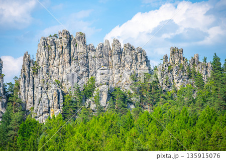 Rock formations rise high above green trees under a blue sky. Clouds float in the background while nature surrounds the area. This scene shows the beauty of the outdoors. Rock formations rise high above green trees under a blue sky. Clouds float in the background while nature surrounds the area. This scene shows the beauty of the outdoors. 135915076