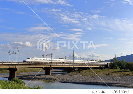 川を渡る白い新幹線と広大な青空 135915566