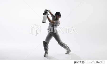 Female cricket player swinging bat during attacking shot in studio. Female cricket player swinging bat during attacking shot in studio. 135916716