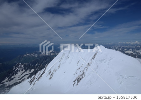 A stunning rock formation covered in snow, set against a clear blue sky with fluffy clouds in the background, creating a peaceful and breathtaking mountain landscape. A stunning rock formation covered in snow, set against a clear blue sky with fluffy clouds in the background, creating a peaceful and breathtaking mountain landscape. 135917330