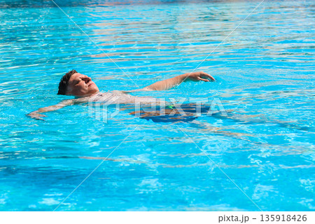 Adult Man Floating on His Back in the Pool of an Egyptian Hotel, Enjoying a Relaxing Day Under the Sun in a Tropical Paradise 135918426