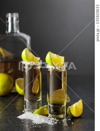 Tequila shots with salt and lime slices on a black stone table. Tequila shots with salt and lime slices on a black stone table. 135920633