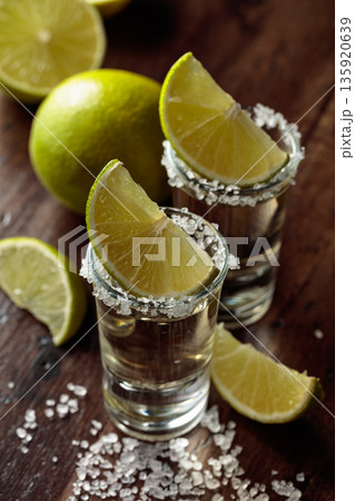 Tequila with salt and lime slices on an old wooden table. Tequila with salt and lime slices on an old wooden table. 135920639