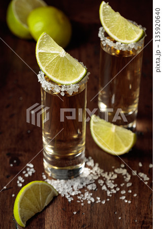 Tequila with salt and lime slices on an old wooden table. Tequila with salt and lime slices on an old wooden table. 135920640