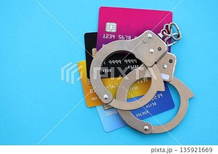 Various credit cards and police handcuffs bracelets on blue background. Concept of banking risks, scam and card skimming Various credit cards and police handcuffs bracelets on blue background. Concept of banking risks, scam and card skimming 135921669