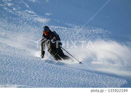 Skier carving through fresh powder on a snowy slope with protective gear and dynamic stance 135922194