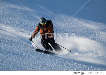 Skier carving a high-speed line down a snowy mountain slope in fresh backcountry powder 135922199