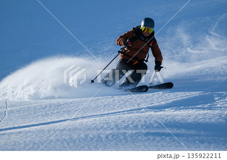 Skier carving through fresh powder on a bright mountain slope 135922211