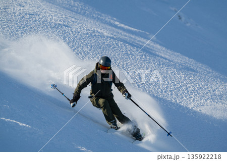 Skier carving through fresh powder on a steep off-piste slope under bright daylight Skier carving through fresh powder on a steep off-piste slope under bright daylight 135922218