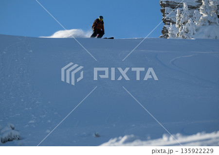 Skier on a snowy slope at crest ready to descend in an off-piste alpine freeride scene Skier on a snowy slope at crest ready to descend in an off-piste alpine freeride scene 135922229