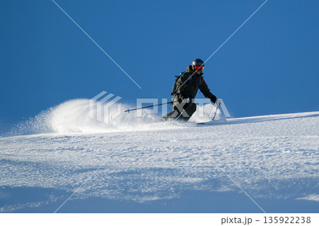 Skier carving a turn on fresh powder under a clear blue sky in the mountains 135922238