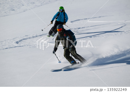 Two skiers carve through fresh powder on a snowy mountain slope during a freeride descent Two skiers carve through fresh powder on a snowy mountain slope during a freeride descent 135922249