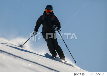 Skier carving down a snowy slope with helmet and goggles on a bright blue day Skier carving down a snowy slope with helmet and goggles on a bright blue day 135922263