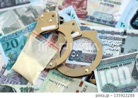 Egyptian pound currency money bills and cocaine pack with handcuffs close up. The concept of drug crimes Egyptian pound currency money bills and cocaine pack with handcuffs close up. The concept of drug crimes 135922288
