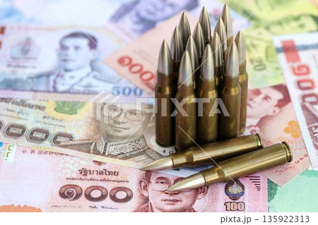 Thai baht currency money bills and rifle bullets close up. The concept of warfare and gun selling 135922313