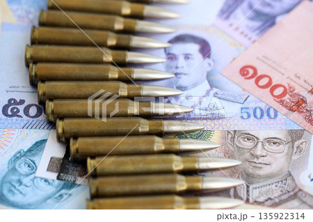 Thai baht currency money bills and rifle bullets close up. The concept of warfare and gun selling 135922314
