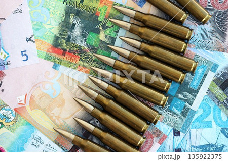 Kuwaiti dinar currency money bills and rifle bullets close up. The concept of warfare and gun selling Kuwaiti dinar currency money bills and rifle bullets close up. The concept of warfare and gun selling 135922375