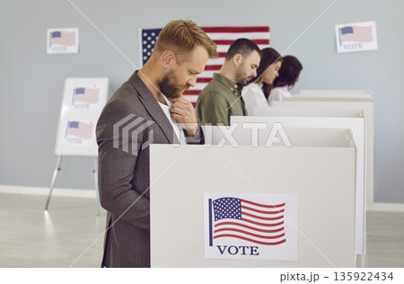 Male citizen in polling booth with American flag thinking which candidate to vote for 135922434