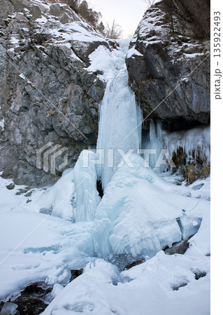 Frozen waterfall cascading down a Rocky Gorge. Winter landscape with natural ice formation. Winter nature adventure and cold environment concept. Frozen waterfall cascading down a Rocky Gorge. Winter landscape with natural ice formation. Winter nature adventure and cold environment concept. 135922493