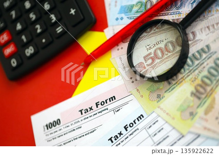 Vietnamese dong money bills and calculator with tax form on flag close up. Taxation and accounting concept Vietnamese dong money bills and calculator with tax form on flag close up. Taxation and accounting concept 135922622