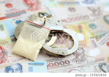 Vietnamese dong currency money bills and cocaine pack with handcuffs close up. The concept of drug crimes Vietnamese dong currency money bills and cocaine pack with handcuffs close up. The concept of drug crimes 135922638