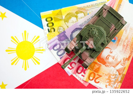 Philippines peso currency money bills and toy tank on flag close up. The concept of army funds and weapons sales Philippines peso currency money bills and toy tank on flag close up. The concept of army funds and weapons sales 135922652