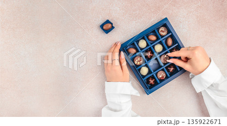 Hands selecting chocolate praline from luxury gift box with copy space 135922671