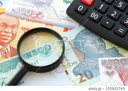 Nigerian naira currency money bills and calculator with magnifying glass close up. The concept of taxation and money count Nigerian naira currency money bills and calculator with magnifying glass close up. The concept of taxation and money count 135922743