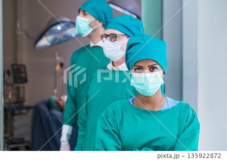 Portrait of Multi-Cultural surgical doctor team in green coat, arms crossed, and standing in front of emergency surgical room. Look at camera. Portrait of Multi-Cultural surgical doctor team in green coat, arms crossed, and standing in front of emergency surgical room. Look at camera. 135922872