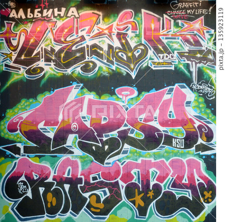 The old wall decorated with paint stains in the style of street art culture. Colorful background of full graffiti painting artwork with bright aerosol outlines on wall. Colored background texture 135923119