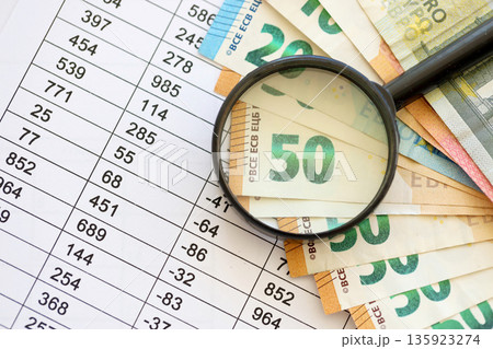 Business and savings concept with many euro money bills and magnifying glass close up 135923274