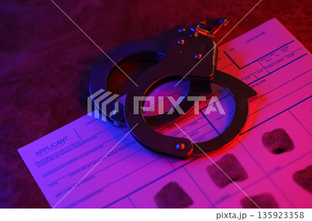 Applicant or fingerprints card with police handcuffs on table in dark room close up 135923358