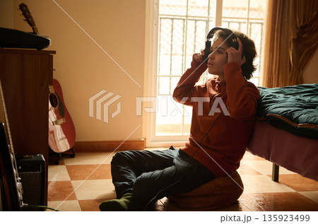Teenage Boy With Headphones Exploring Music In A Cozy Bedroom Studio Setup At Home Teenage Boy With Headphones Exploring Music In A Cozy Bedroom Studio Setup At Home 135923499