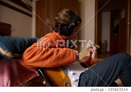 Teen Guitar Player Relaxing At Home: Cozy Indoor Scene With Headphones And Electric Guitar Teen Guitar Player Relaxing At Home: Cozy Indoor Scene With Headphones And Electric Guitar 135923514