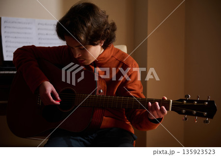 Teenage Boy Playing Acoustic Guitar In Warm Room, Focused On Music Hobby Teenage Boy Playing Acoustic Guitar In Warm Room, Focused On Music Hobby 135923523