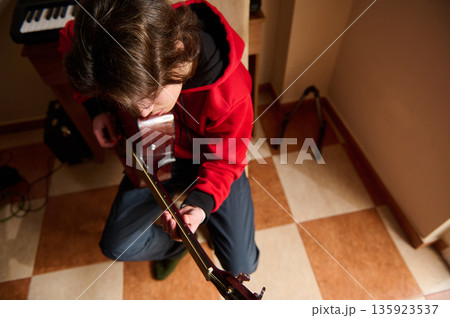 Teen Boy In Red Hoodie Playing Guitar Indoors, Focused Music Hobby Teen Boy In Red Hoodie Playing Guitar Indoors, Focused Music Hobby 135923537