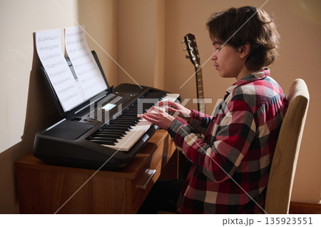 Teenage Boy Playing Piano At Home With Sheet Music And Guitar In Background Teenage Boy Playing Piano At Home With Sheet Music And Guitar In Background 135923551