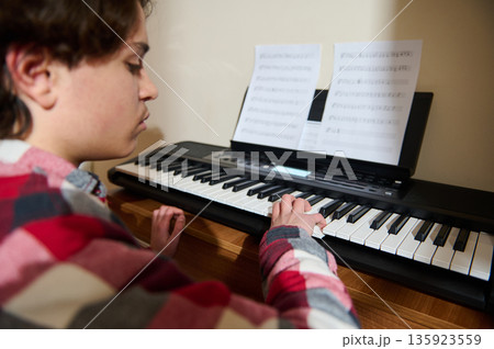 Teenage Boy Plays Piano At Home With Sheet Music In Front Of Keyboard 135923559