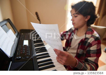 Teenage Boy Playing Piano With Sheet Music In Home Studio While Practicing Teenage Boy Playing Piano With Sheet Music In Home Studio While Practicing 135923564