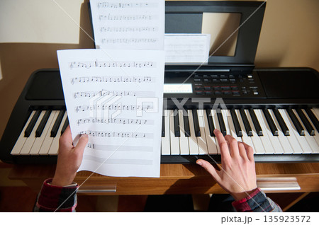 Teenage Pianist Playing Keyboard With Sheet Music On Stand And Hands On Keys 135923572