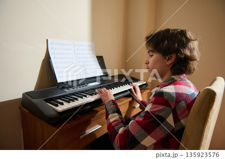 Teenage Boy Plays Keyboard Piano At Home With Sheet Music On Stand Teenage Boy Plays Keyboard Piano At Home With Sheet Music On Stand 135923576