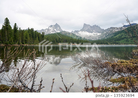 Peaceful mountain lake with surrounding forest and snowy peaks Peaceful mountain lake with surrounding forest and snowy peaks 135923694
