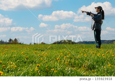 Woman holding smartphone and pointing in field of yellow dandelions 135923918