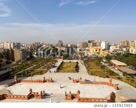 Aerial view of Heliopolis district in Cairo. The scene includes green parks, modern buildings, and clear blue skies. Urban landscape with palm trees and pathways. Aerial view of Heliopolis district in Cairo. The scene includes green parks, modern buildings, and clear blue skies. Urban landscape with palm trees and pathways. 135923983