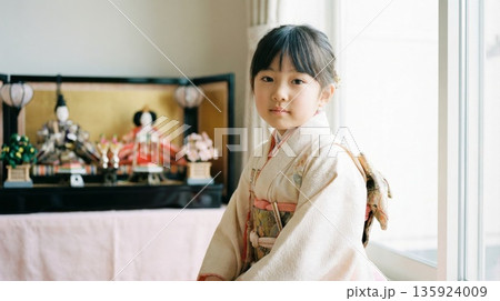 窓辺に飾られた立派な雛人形の前で着物を着てカメラを見つめる美しい日本人の少女 窓辺に飾られた立派な雛人形の前で着物を着てカメラを見つめる美しい日本人の少女 135924009