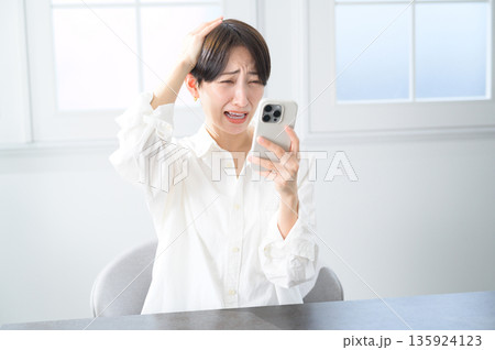 スマホを見てショックを受けるショートヘアの女性 スマホを見てショックを受けるショートヘアの女性 135924123
