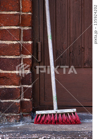 Outdoor close up of a push broom with red bristles leaning on a concrete step next to a brick wall Outdoor close up of a push broom with red bristles leaning on a concrete step next to a brick wall 135924202