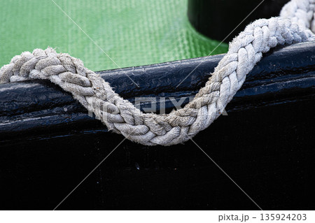 Close up of a braided rope handle attached hanging on a black boat side with a green textured floor Close up of a braided rope handle attached hanging on a black boat side with a green textured floor 135924203