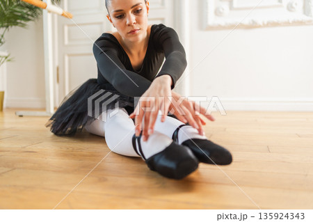Young ballerina in tutu skirt stretching practicing ballet positions dancing in dance class. Young classical dancer woman in dance studio. Ballet class training Ballet school concept 135924343